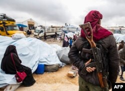 FILE - A member of Kurdish security forces watches as families load their belongings onto trucks before leaving the Kurdish-run al-Hol camp, in the Hasakah governorate in northeastern Syria, Nov. 16, 2020.
