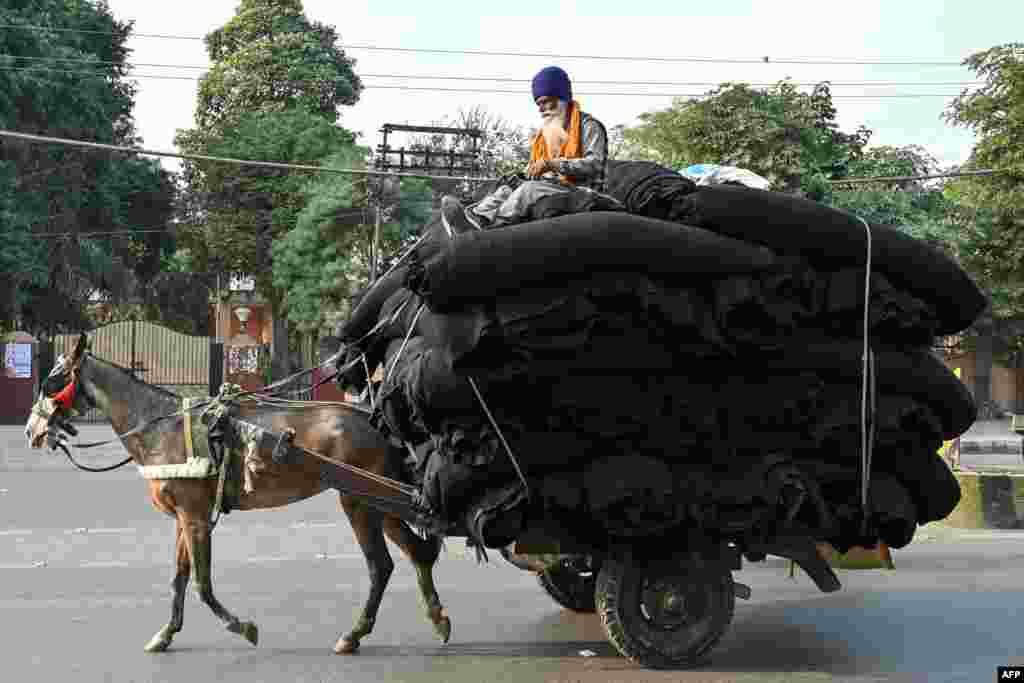 A man sits atop blankets as he transports them on a horse-drawn cart through a street in Amritsar, India.