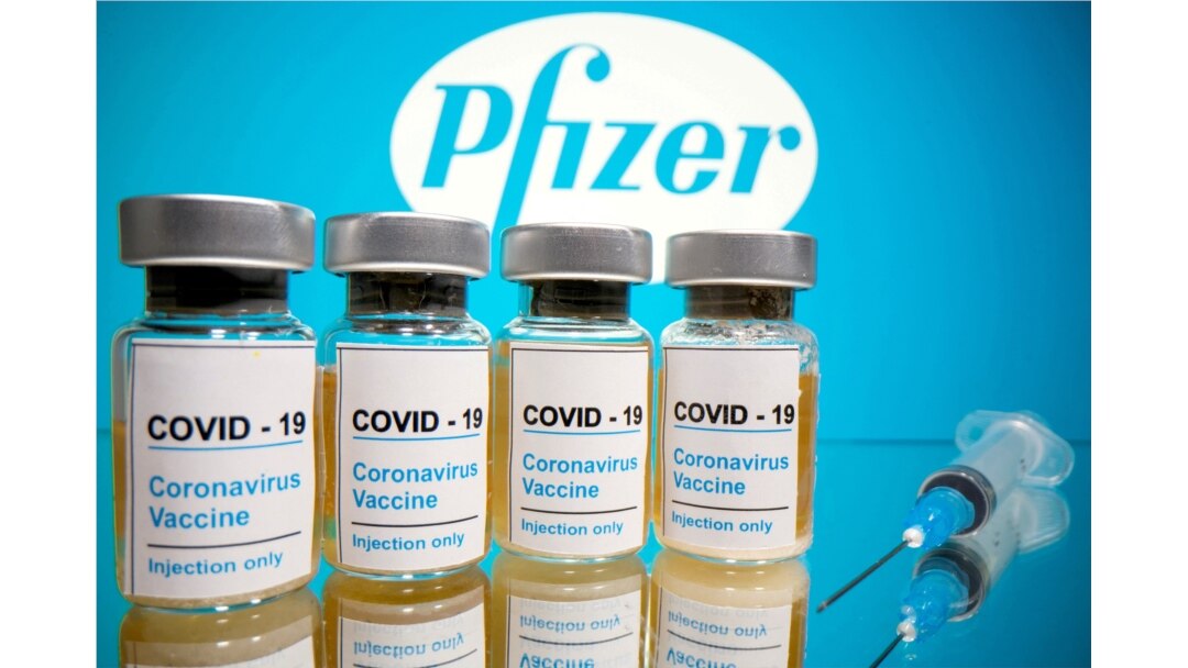 Los frascos con una etiqueta que dice "COVID-19 y una jeringa médica se ven frente al logotipo de Pfizer, 31 de octubre de 2020.