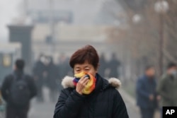 FILE - In this Tuesday, Dec. 20, 2016, file photo, a woman uses a scarf to cover her mouth for protection against the air pollution as she walks on a street in Beijing, China.