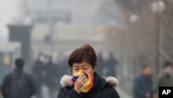 FILE - In this Tuesday, Dec. 20, 2016, file photo, a woman uses a scarf to cover her mouth for protection against the air pollution as she walks on a street in Beijing, China.