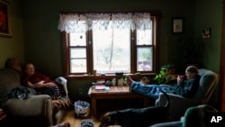 Caroline Clarin, right, and her wife, Sheril Raymond, sit in their living room with their dogs, Daisy, left, and Iorek, in Dalton, Minn., Oct. 27, 2021.