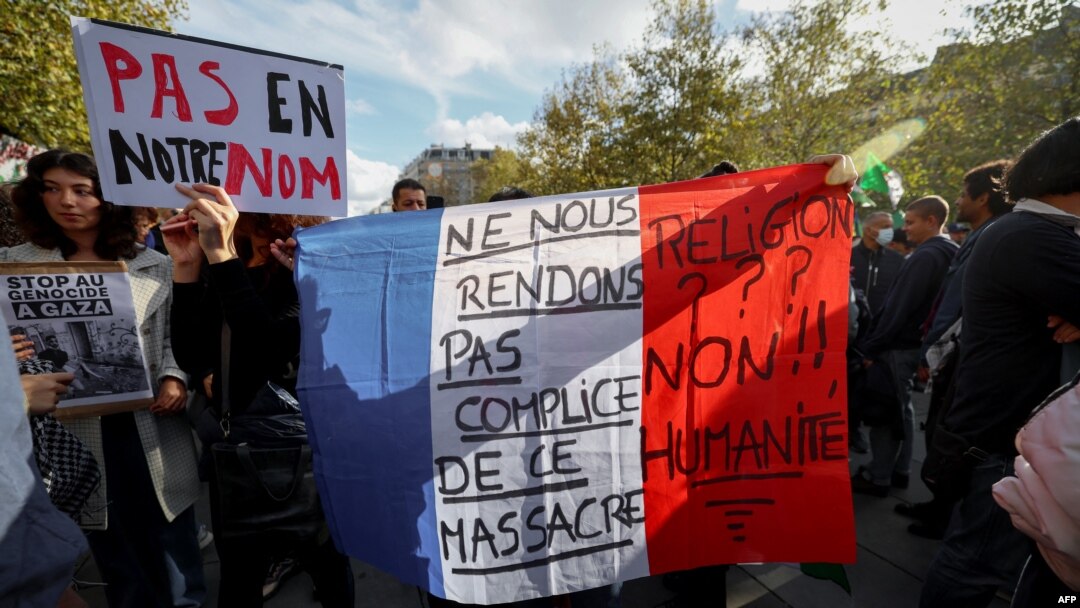 FILE - A protestor holds the national flag of France with the words "Let's not be complicit in the massacre" as they gather at Place de la Republique during a demonstration calling for peace in Gaza in Paris, on October 22, 2023.
