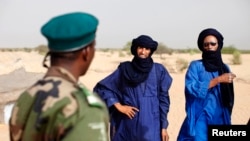 FILE - A Malian soldier speaks with Tuareg men in the village of Tashek, outside Timbuktu, July 27, 2013. 