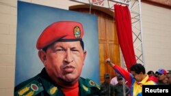 ຮອງປະທານາທິບໍດີ ເວເນຊູເອລາ ທ່ານ Nicolas Maduro ກໍາລັງ ຍົກກໍາປັ້ນໃຫ້ກຽດແກ່ ຮູບແຕ້ມ ປະທານາທິບໍດີ Hugo Chavez