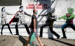 FILE - A man wearing a protective face mask walks past a mural depicting a tug-of-war between health workers and President Jair Bolsonaro, with a message that reads in Portuguese: "Which side are you on?" in Sao Paulo, Brazil, June 19, 2020.