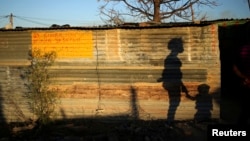 FILE - The shadows of a mother and child are cast on a shack in Marikana's Nkaneng township in Rustenburg, northwest of Johannesburg, South Africa, Aug. 15, 2013.