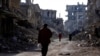 FILE - People walk past damaged buildings at the Yarmouk Palestinian refugee camp on the southern outskirts of Damascus, Syria, Dec. 2, 2020. 