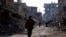 FILE - People walk past damaged buildings at the Yarmouk Palestinian refugee camp on the southern outskirts of Damascus, Syria, Dec. 2, 2020. 