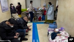 People wearing face masks take a rest as they tend to their elderly relatives rest along a corridor of the emergency ward to provide intravenous drips at a hospital in Beijing, Jan. 3, 2023.