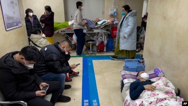 People wearing face masks take a rest as they tend to their elderly relatives rest along a corridor of the emergency ward to provide intravenous drips at a hospital in Beijing, Jan. 3, 2023.