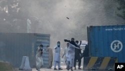 Protesters hurl stones towards police who fired tear gas shell, as they march toward the French Embassy during a rally against French President Emmanuel Macron in Islamabad, Pakistan, Oct. 30, 2020.