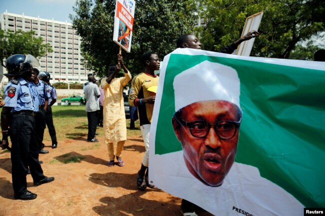 FILE - Supporters of President Muhammadu Buhari rally in support of his administration as police officers look on, at the Unity fountain in Abuja, Nigeria, Aug. 11, 2017.