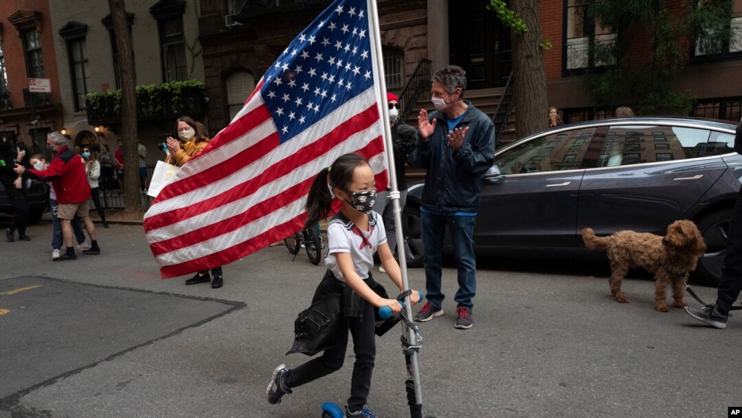 A girl parades up and down her block with a U.S. flag on her scooter, in the Greenwich Village neighborhood, during a partial easing of coronavirus restrictions in New York, May 14, 2020.