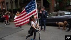 A girl parades up and down her block with a U.S. flag on her scooter, in the Greenwich Village neighborhood, during a partial easing of coronavirus restrictions in New York, May 14, 2020.