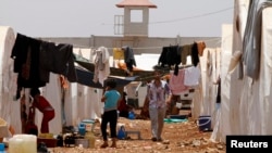 FILE - Syrian refugees walk under clothing lines at the Bab Al-Salam refugee camp in Azaz, near the Syrian-Turkish border, June 9, 2013. 