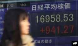 FILE - A woman walks past an electronic stock board showing Japan's Nikkei 225.