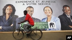 A cyclist rides past a campaign poster of candidates of the Democratic Party of Ivory Coast in Abidjan December 6, 2011. The slogan on the poster reads "Experience and youth at your service."