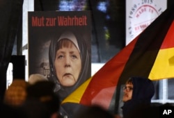FILE - A poster with the writing "Courage to speak the truth" depicts German Chancellor Angela Merkel wearing a veil during a demonstration of the Legida anti-Islamization movement, an offshoot of Pegida, in Leipzig, Jan. 30, 2015.