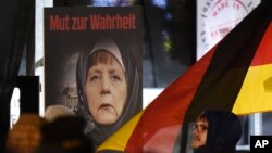 ARSIP – Sebuah poster dengan bunyi “Keberanian untuk Berbicara Jujur” menggambarkan Kanselir Jerman, Angela Merkel, mengenakan hijab di depan gedung Reichstag dengan bulan sabit di atasnya dalam sebuah demonstrain gerakan anti Islamisasi, Legida, gerakan turunan Pegida, di Leipzing, Jeman, 30 Januari 2015 (foto: AP Photo/Jens Meyer)