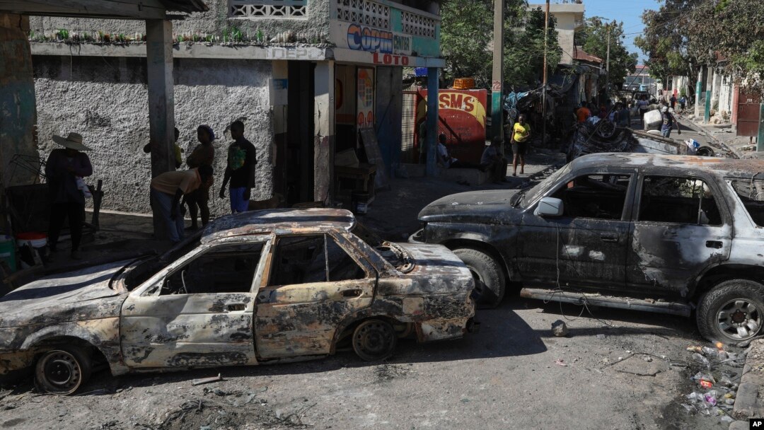 FILE - Residents walk past cars set on fire by armed gangs in the Poste Marchand neighborhood of Port-au-Prince, Haiti, Dec. 10, 2024.
