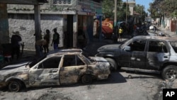 FILE - Residents walk past cars set on fire by armed gangs in the Poste Marchand neighborhood of Port-au-Prince, Haiti, Dec. 10, 2024.