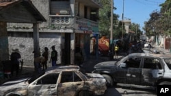 Residents walk past cars set on fire by armed gangs in the Poste Marchand neighborhood of Port-au-Prince, Haiti, Dec. 10, 2024. 