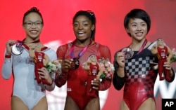 FILE - Gold medalist Simone Biles of the U.S., center, silver medalist Morgan Hurd of the U.S., left, and bronze medalist Japan's Mai Murakami pose after their floor exercise on the second and last day of the apparatus finals of the Gymnastics World Championships at the Aspire Dome in Doha, Qatar, Nov. 3, 2018.