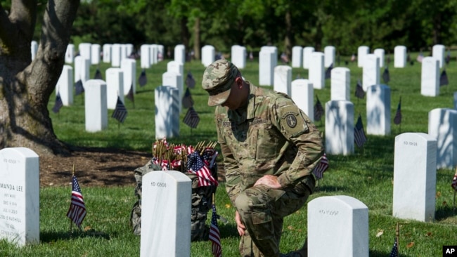 Un soldado coloca una badera frente a la tumba de un soldado caído en acción y sepultado en el Cementerio Nacioal de Arlington, Virginia.