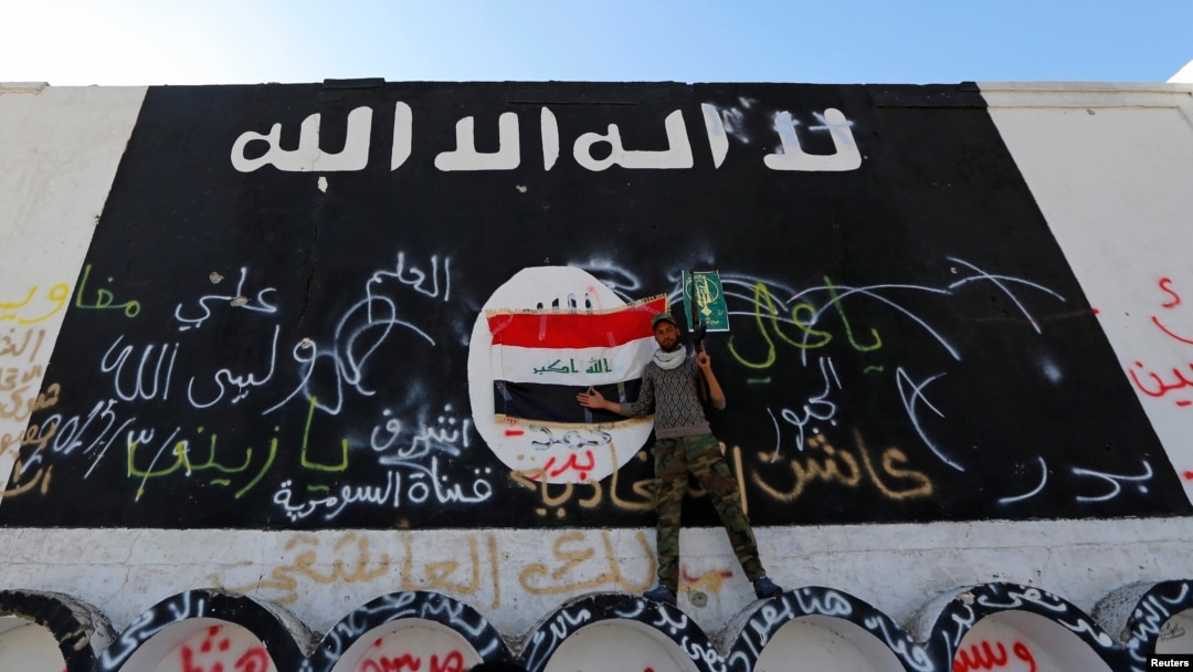 Seorang anggota milisia Hashid Shaabi berdiri dekat dinding yang digambari bendera ISIS di kota al-Alam, Irak. (Reuters/Thaier Al-Sudani)