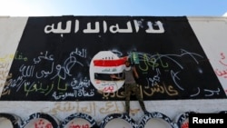 FILE - A member of militias known as Hashid Shaabi stands next to a wall painted with the black flag commonly used by Islamic State militants, in the town of al-Alam, Iraq.