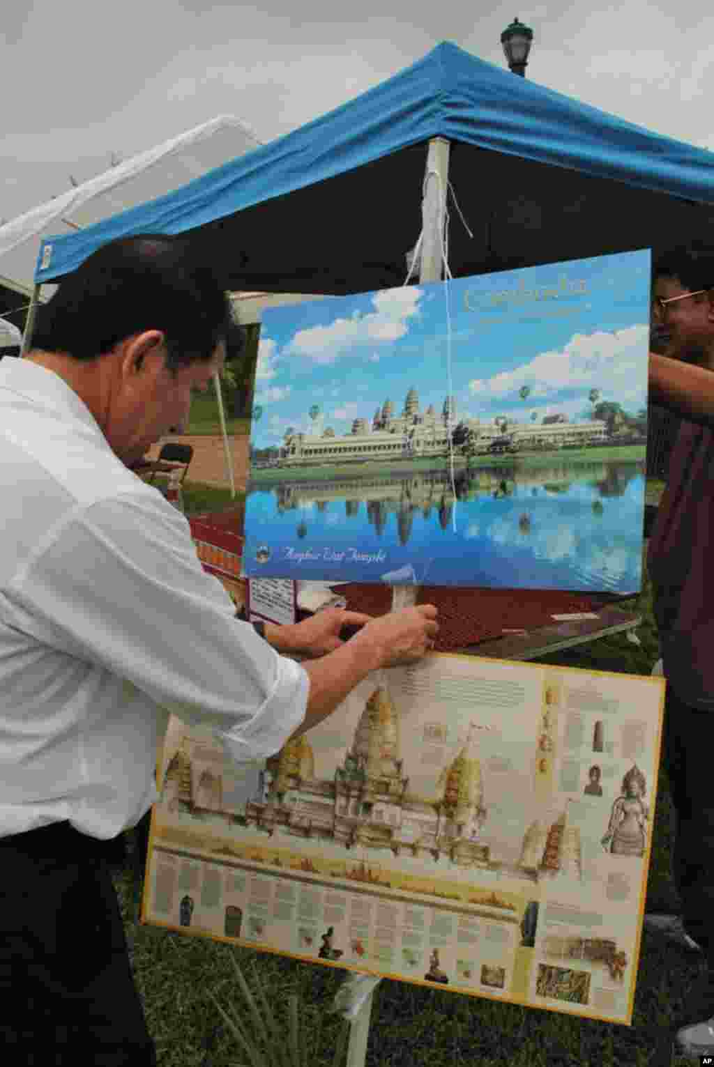 Mr. Seng Chao (ចៅ សេង), Executive Director of Cambodian Senior Citizens, readies a National Geographic poster of Angkor Wat for his organization's stall at the festival. His organization is among several civil groups taking part in the event.