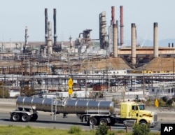 FILE - In this March 9, 2010, photo, a tanker truck passes an oil refinery in Richmond, California. Vowing to keep the United States on track to meet its emissions-cutting target, an alliance of states, cities and businesses have pledged to stay in the