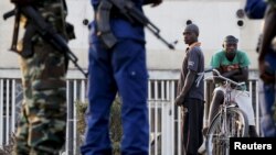 FILE - Residents look on as police and soldiers guard a voting station in Burundi's capital, Bujumbura, during the country's presidential elections, July 21, 2015.