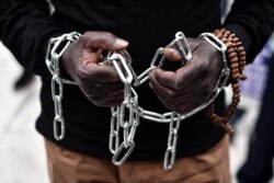 FILE - An African migrant with his hands chained takes part in a march toward the offices of the European Union during a demonstration on Dec. 2, 2017, in central Athens, protesting against the slavery of migrants in Libya.