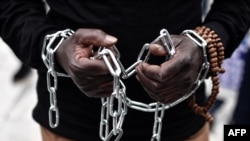FILE - An African migrant with his hands chained takes part in a march toward the offices of the European Union during a demonstration on Dec. 2, 2017, in central Athens, protesting against the slavery of migrants in Libya.