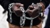 FILE - An African migrant with his hands chained takes part in a march toward the offices of the European Union during a demonstration on Dec. 2, 2017, in central Athens, protesting against the slavery of migrants in Libya.