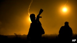 FILE - A U.S.-backed Syrian Democratic Forces (SDF) fighter watches illumination rounds light up Baghuz, Syria, as the last pocket of Islamic State militants is attacked on March 12, 2019. 