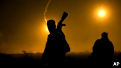 A U.S.-backed Syrian Democratic Forces (SDF) fighter watches illumination rounds light up Baghuz, Syria, as the last pocket of Islamic State militants is attacked, March 12, 2019. 
