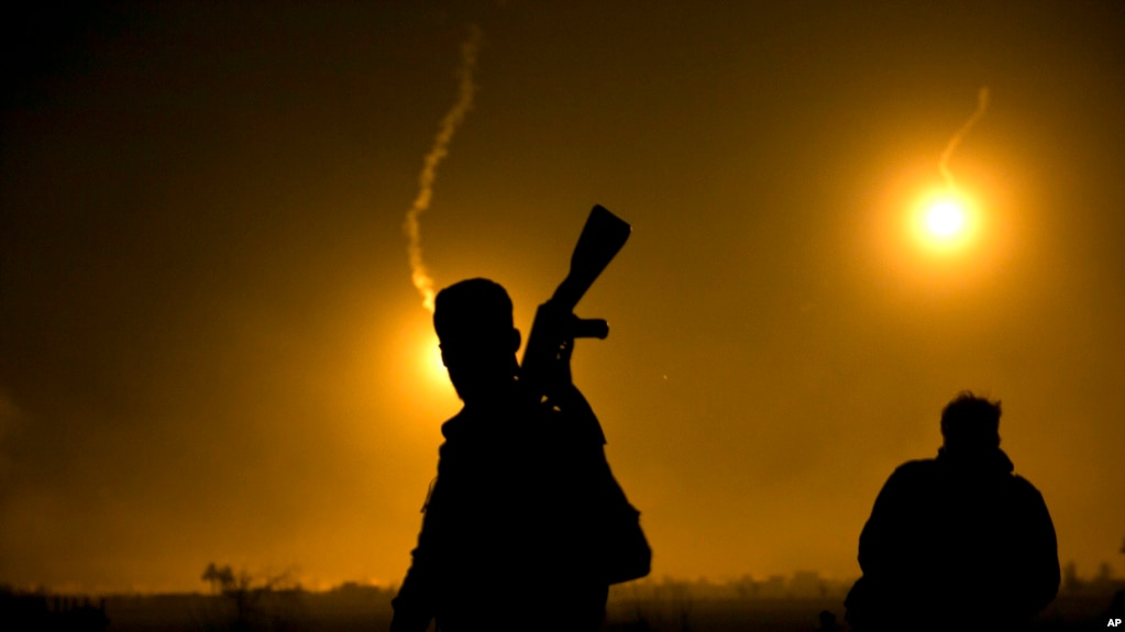 FILE - A U.S.-backed Syrian Democratic Forces fighter watches illumination rounds light up Baghuz, Syria, as the last pocket of Islamic State militants is attacked on March 12, 2019. 