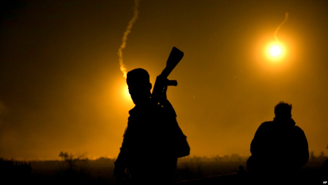 A U.S.-backed Syrian Democratic Forces (SDF) fighter watches illumination rounds light up Baghuz, Syria, as the last pocket of Islamic State militants is attacked on March 12, 2019. 