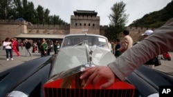 FILE - A man places his hand near the logo of a Rolls Royce at the Shuiguan Great Wall on the outskirts of Beijing, China, Sept. 18, 2011. A new law now tries to coordinate charitable giving by country's richest.