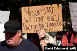 FILE - A person holds up a sign during a rally to address problems in the apartment buildings occupied by people displaced from their home countries in central and South America, Sept. 3, 2024, in Aurora, Colo. (AP Photo/David Zalubowski, File)