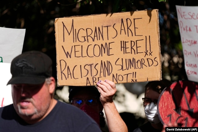 FILE - A person holds up a sign during a rally to address problems in the apartment buildings occupied by people displaced from their home countries in central and South America, Sept. 3, 2024, in Aurora, Colo. (AP Photo/David Zalubowski, File)