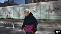 一名中国妇女走过北京一处建筑工地，背后的宣传牌上写着“文明”“民主”“富强”“友善”“诚信”。（法新社 2018年12月4日）