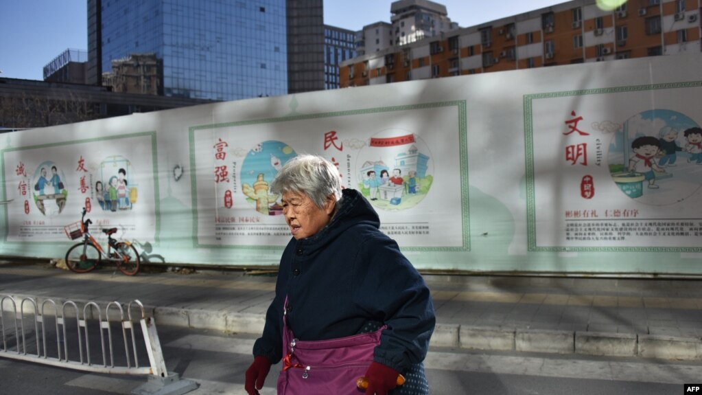 一名中国妇女走过北京一处建筑工地，背后的宣传牌上写着“文明”“民主”“富强”“友善”“诚信”。（法新社 2018年12月4日）(photo:VOA)