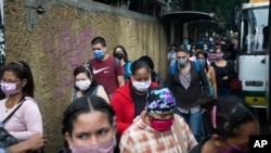 Personas con máscaras faciales en medio de la pandemia de coronavirus se agolpan en una acera cerca de una parada de autobús en Caracas, Venezuela, el lunes 1 de junio de 2020.