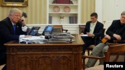 U.S. President Donald Trump, seated at his desk with National Security Advisor Michael Flynn and senior advisor Steve Bannon, right, on the phone in the Oval Office at the White House, Jan. 28, 2017. 