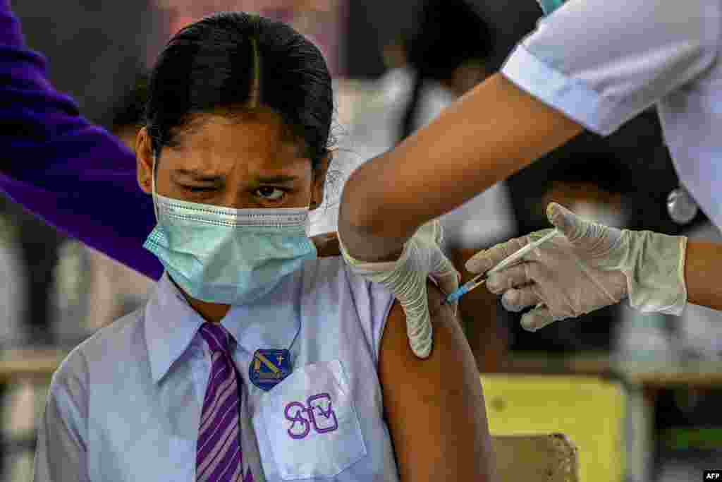 A student reacts as a health worker inoculates her with the dose of Pfizer-BioNTech vaccine against COVID-19 at an educational institution in Colombo, Sri Lanka.