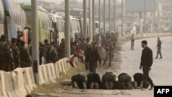 FILE - Syrian regime forces stand near buses while rebel fighters pray as they wait at the entrance of Harasta in Eastern Ghouta, on the outskirts of Damascus, March 22, 2018, after a deal was struck with the rebels in the area to evacuate the town.